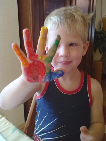 Ein Kind hält eine Hand hoch, die mit Fingerfarben bunt angemalt wurde