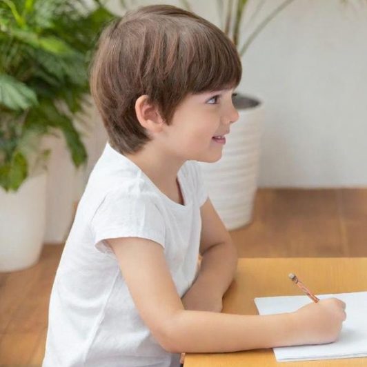 Ein Kind sitzt mit einer Logopädin am Tisch und schreibt.